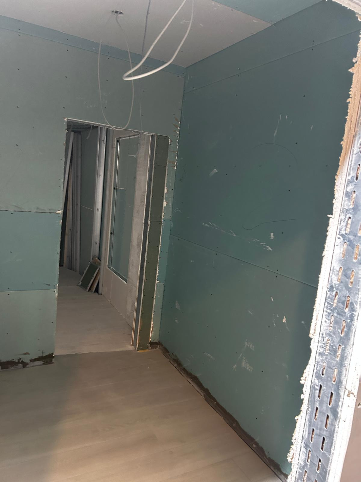 Montaż płyt gipsowo-kartonowych na ścianach i suficie w nowym budynku, widoczne profile metalowe i wystające przewody elektryczne.