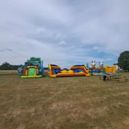 Kompleks dmuchańców w plenerze: zjeżdżalnia z motywem zoo, tor przeszkód i dmuchany plac zabaw z żyrafami, ustawione na trawiastym terenie pod błękitnym niebem z chmurami.