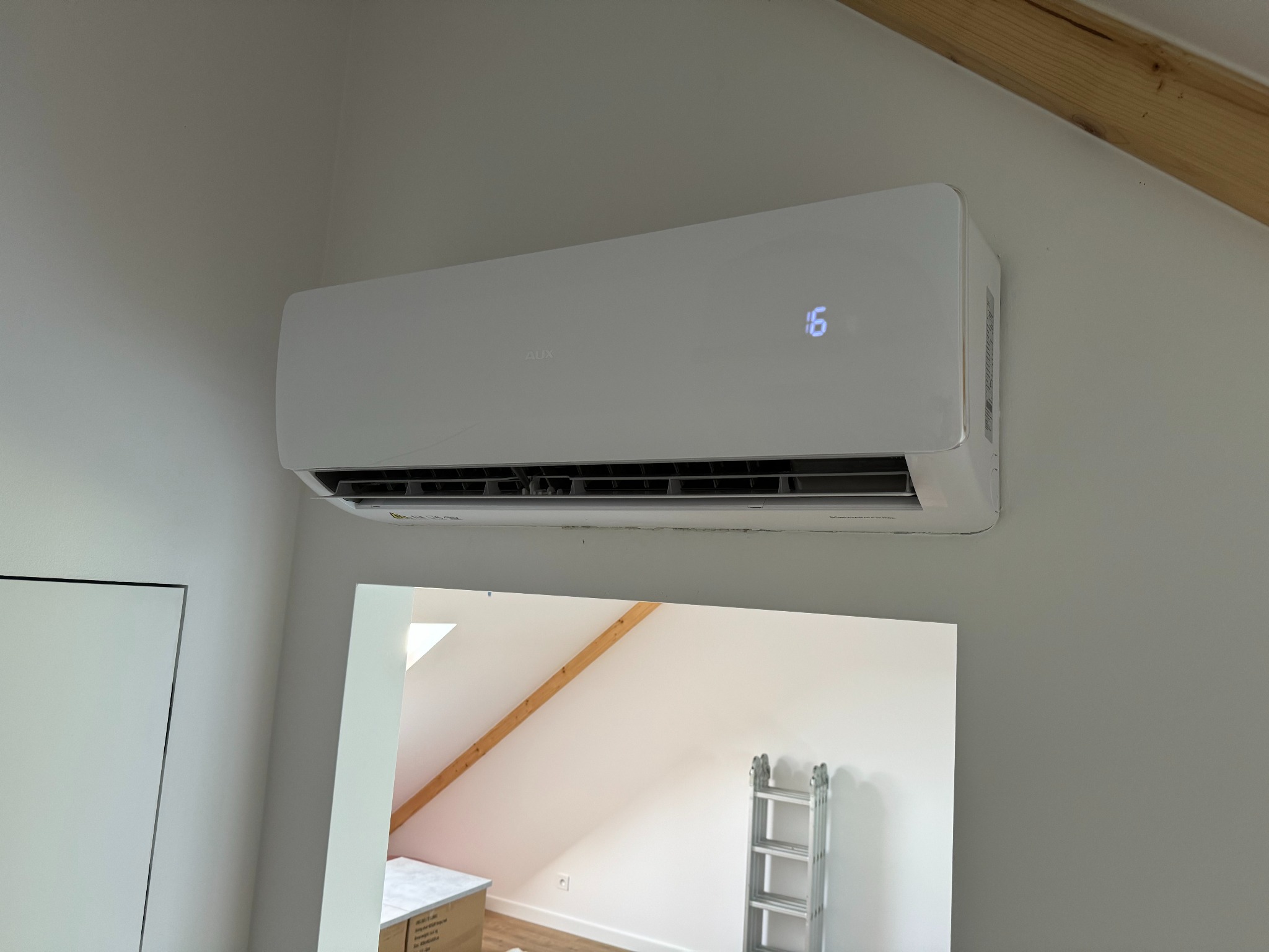 Zamontowany klimatyzator AUX Freedom 5 kW w budynku jednorodzinnym w Rogoźnie, widoczny odbity w lustrze fragment poddasza z drewnianą belką i drabina.