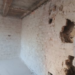 PBSKR.BUD - Wnętrze pomieszczenia po wyburzeniu fragmentu ściany, widoczne odsłonięte cegły i drewniany strop