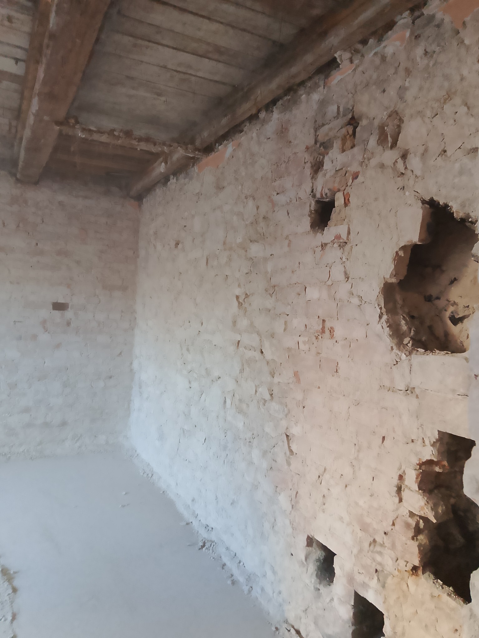 Wnętrze pomieszczenia po wyburzeniu fragmentu ściany, widoczne odsłonięte cegły i drewniany strop