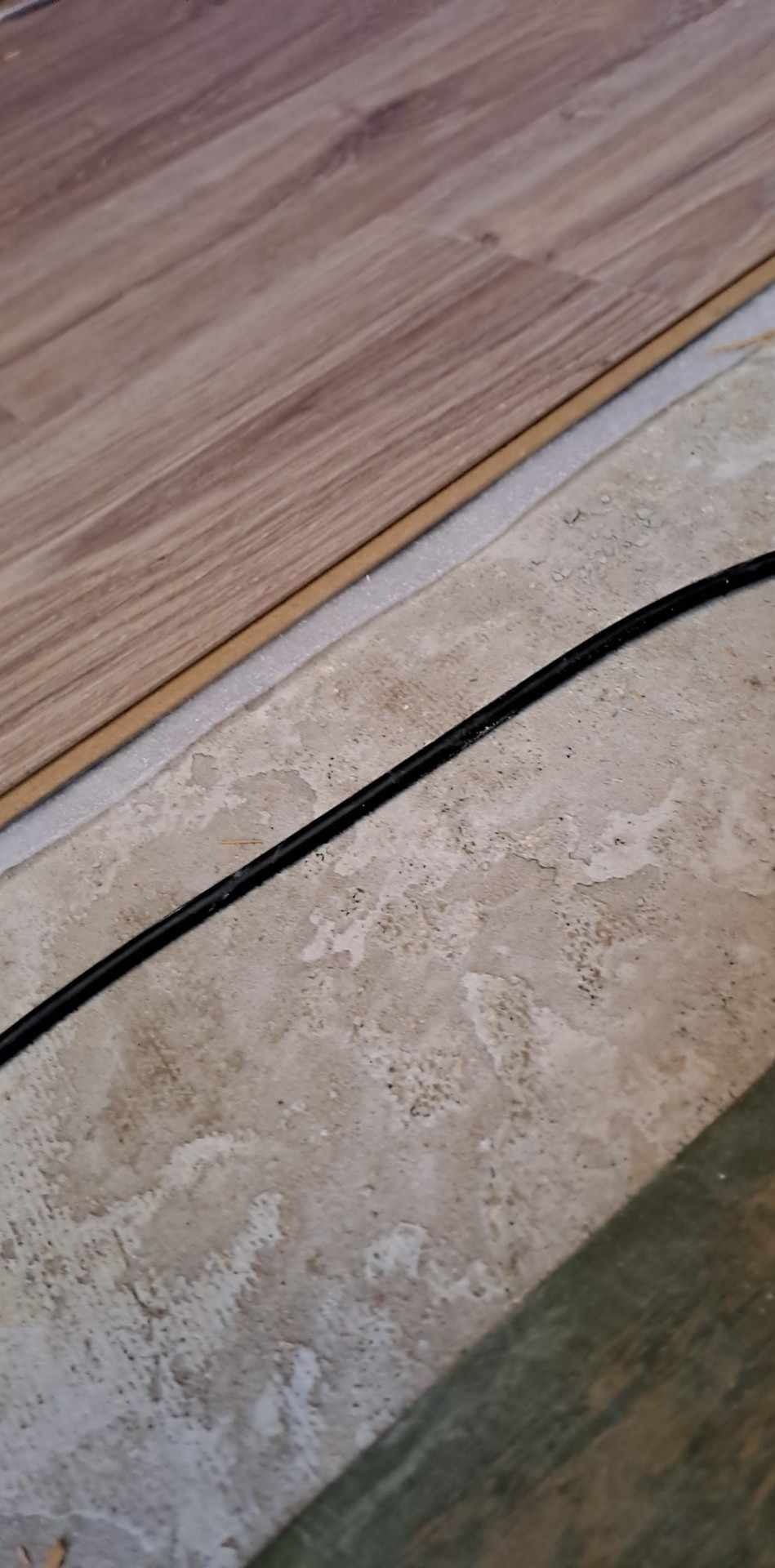 Układanie paneli podłogowych w Częstochowie. Widoczny fragment podłogi z panelami, podkład i kabel elektryczny.