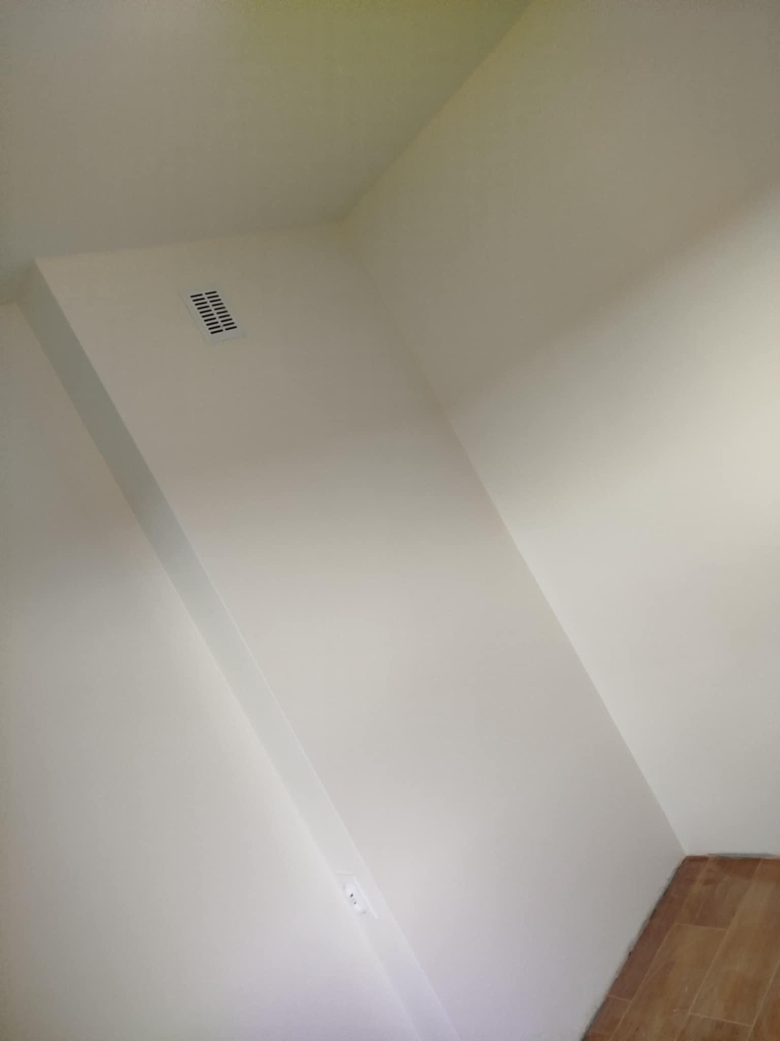 Świeżo pomalowane, białe ściany i sufit w rogu pokoju. Widoczna kratka wentylacyjna. U dołu fragment paneli podłogowych.