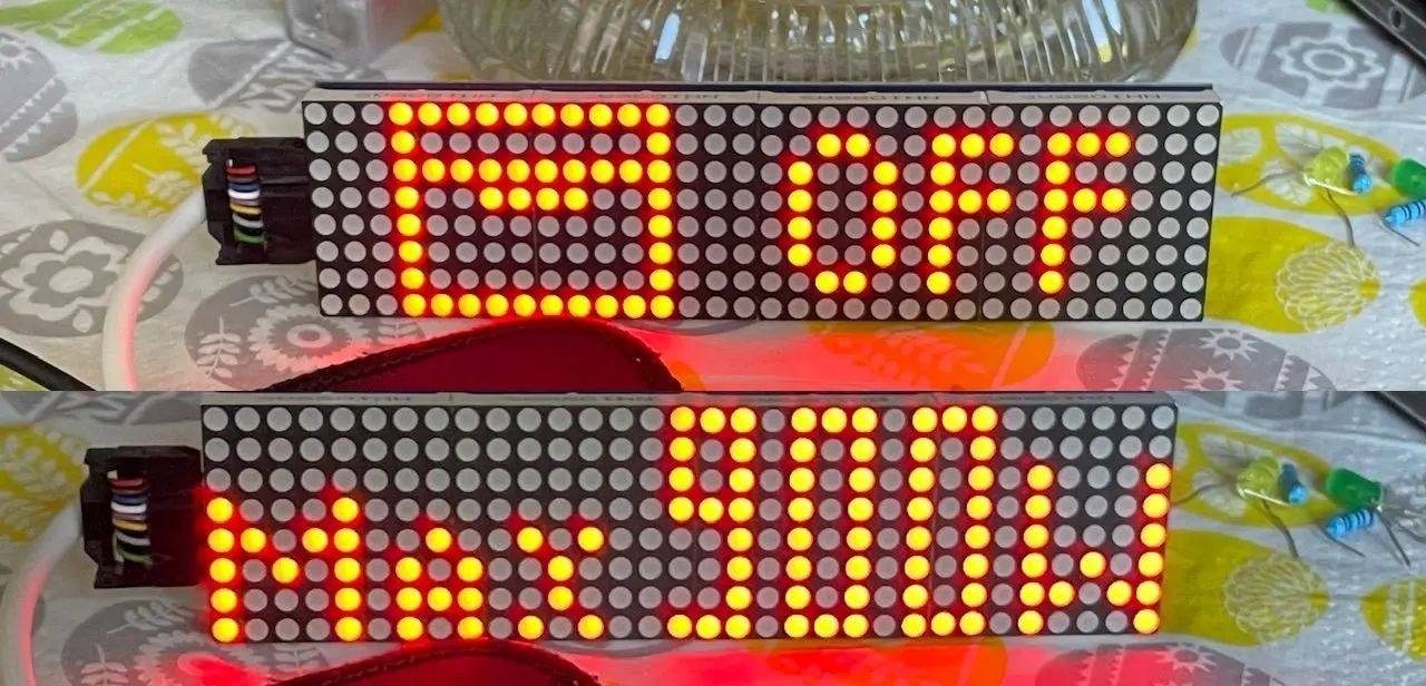 Dwa wyświetlacze LED matrycowe prezentujące tekst, połączone przewodami i komponentami elektronicznymi na wzorzystym tle.