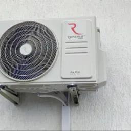 Biała jednostka zewnętrzna klimatyzatora Rotenso Hiro Series zamontowana na kremowej elewacji budynku, widoczna rynna w kolorze brązowym.