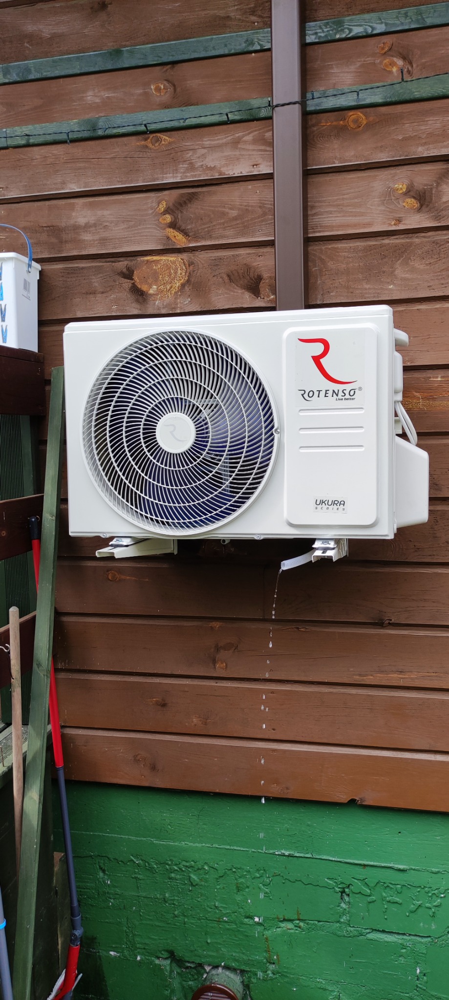 Zamontowany klimatyzator Rotenso Ukura na drewnianej ścianie budynku z widocznym skraplaniem wody z odpływu.