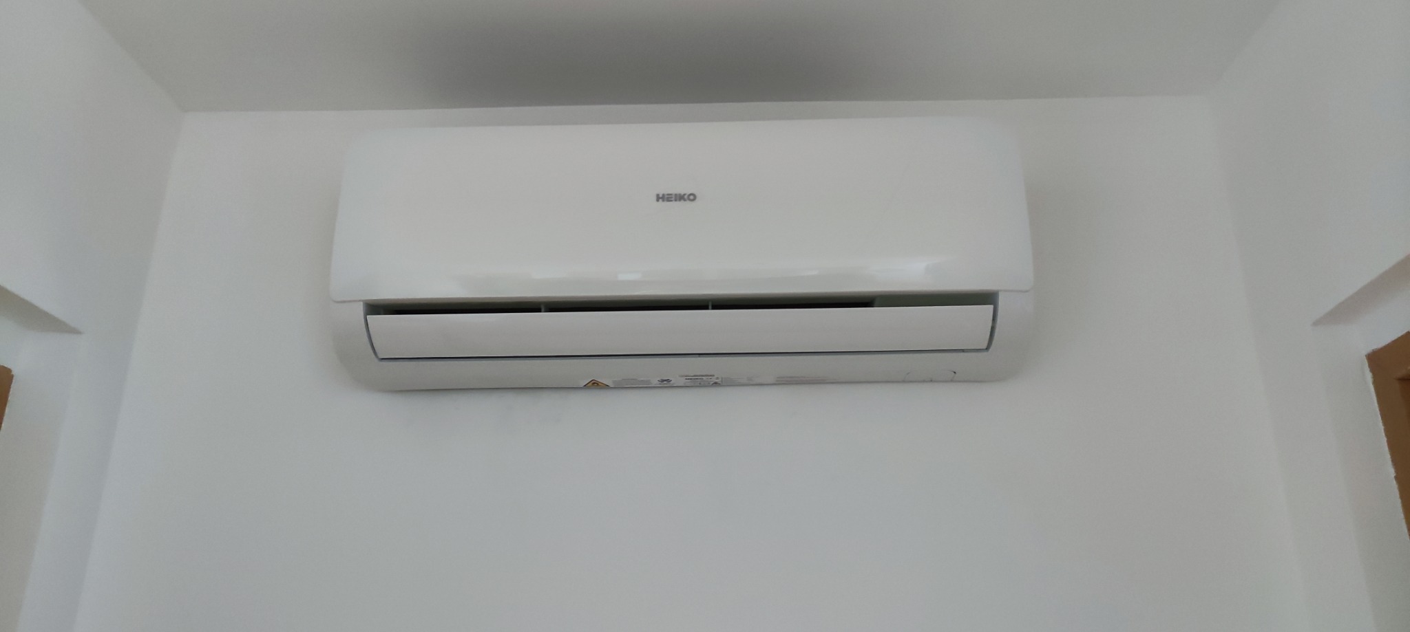 Biały klimatyzator marki Heiko zamontowany na białej ścianie w pomieszczeniu, widoczne detale urządzenia.