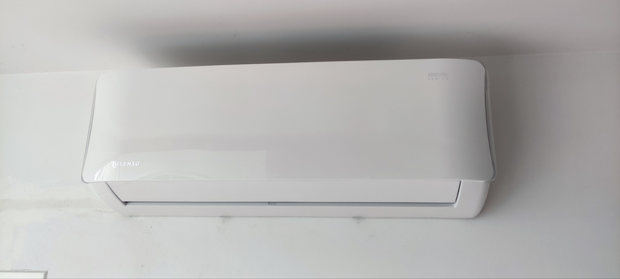 Biała jednostka wewnętrzna klimatyzatora marki Rotenso zamontowana na ścianie, widoczne delikatne ślady na ścianie.