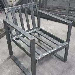 Dav-bud - Metalowy szkielet krzesła z profili kwadratowych, spawane łączenia, surowy wygląd, warsztat w tle.