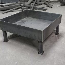 Dav-bud - Surowa, spawana konstrukcja metalowa z kwadratową misą na czterech nogach, w tle nieporządek metalowych profili.
