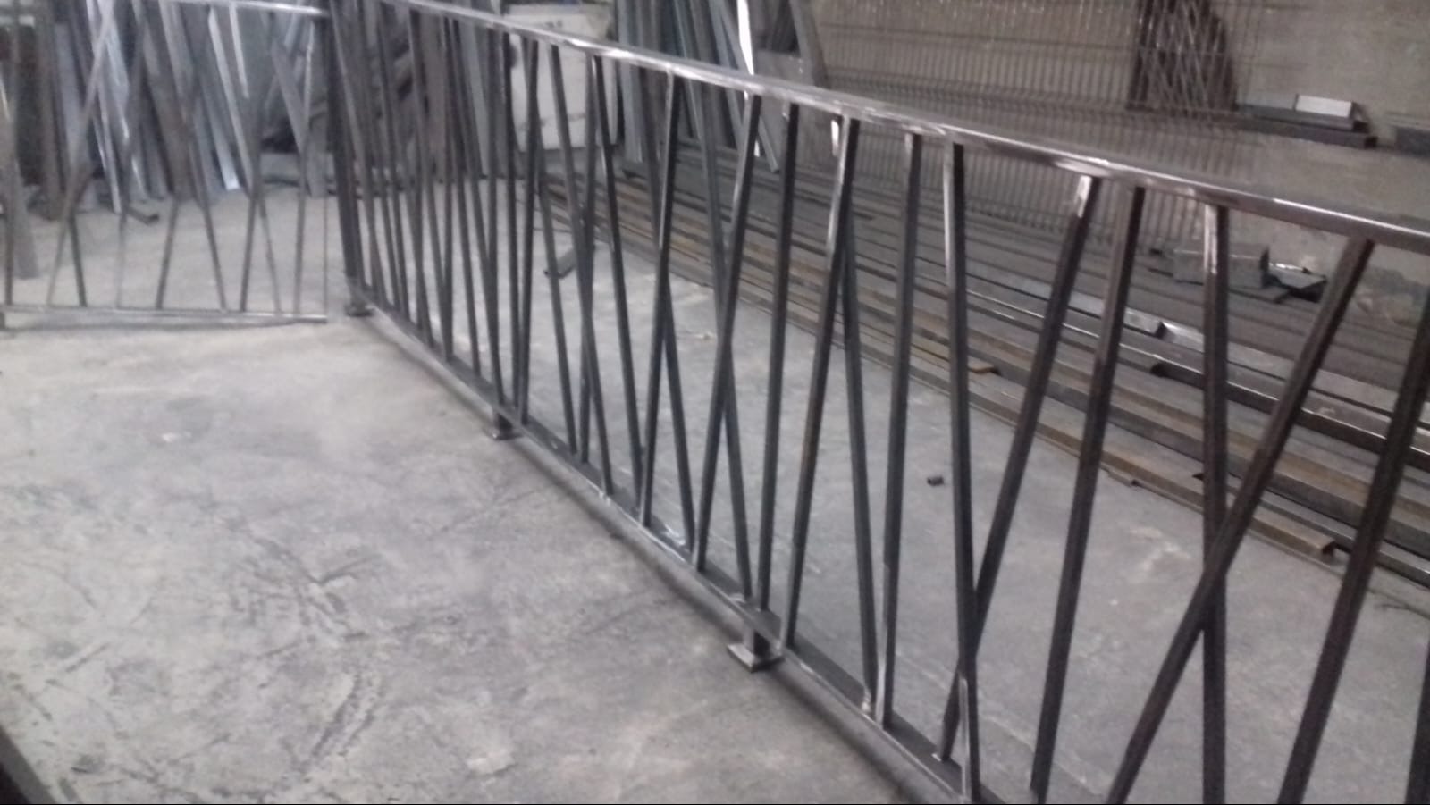 Surowa, spawana konstrukcja metalowa z ukośnymi prętami w warsztacie, widoczne ślady spawania i niedoskonałości wykończenia.