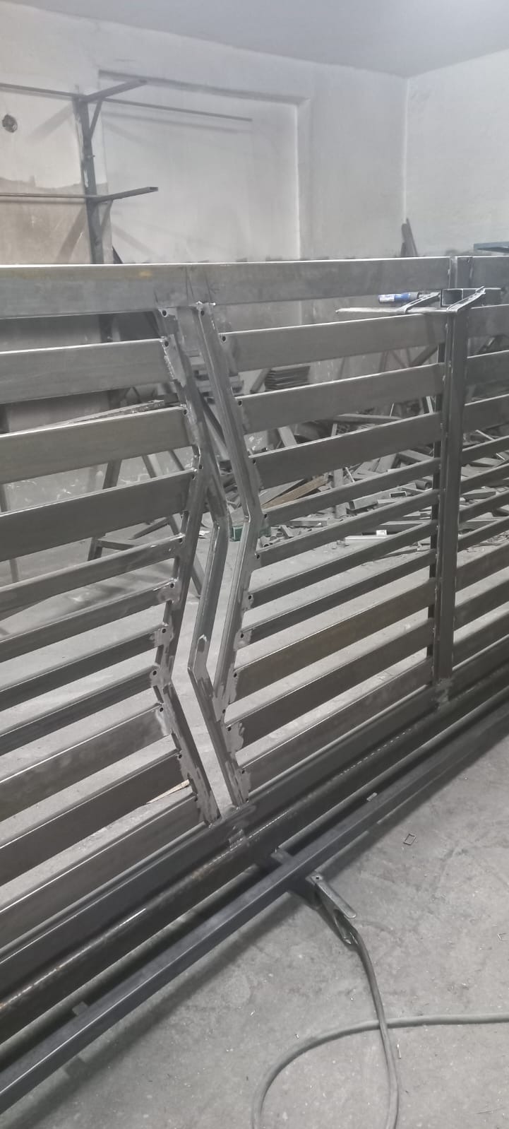 Metalowa brama wjazdowa w trakcie spawania, widoczne spawy i elementy konstrukcyjne, surowy stan wykończenia w warsztacie.