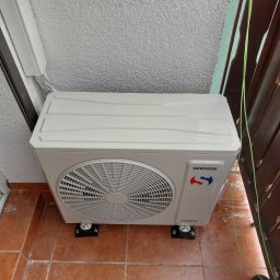 ELEKTROSERWIS Paweł Waligórski - Zewnętrzna jednostka klimatyzacji Sinclair zamontowana na balkonie na pomarańczowych płytkach, widoczne przewody i fragment buta.