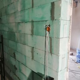 ELEKTROSERWIS Paweł Waligórski - Ściana z betonu komórkowego w trakcie budowy z widoczną puszką instalacyjną i wystającymi przewodami elektrycznymi.