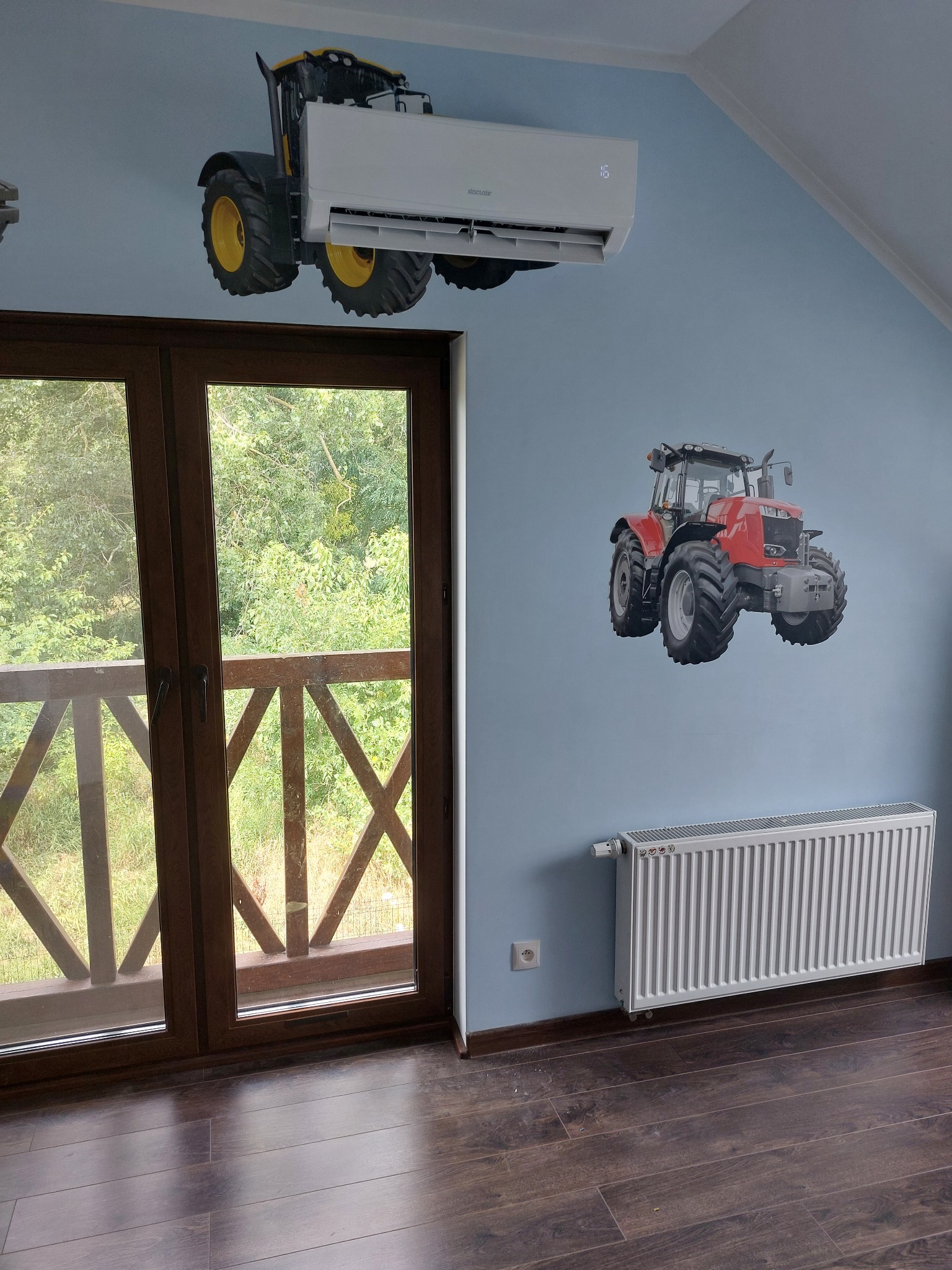 Klimatyzator ścienny zamontowany w pokoju dziecięcym z tapetą w traktory, widok z okna na zieleń.
