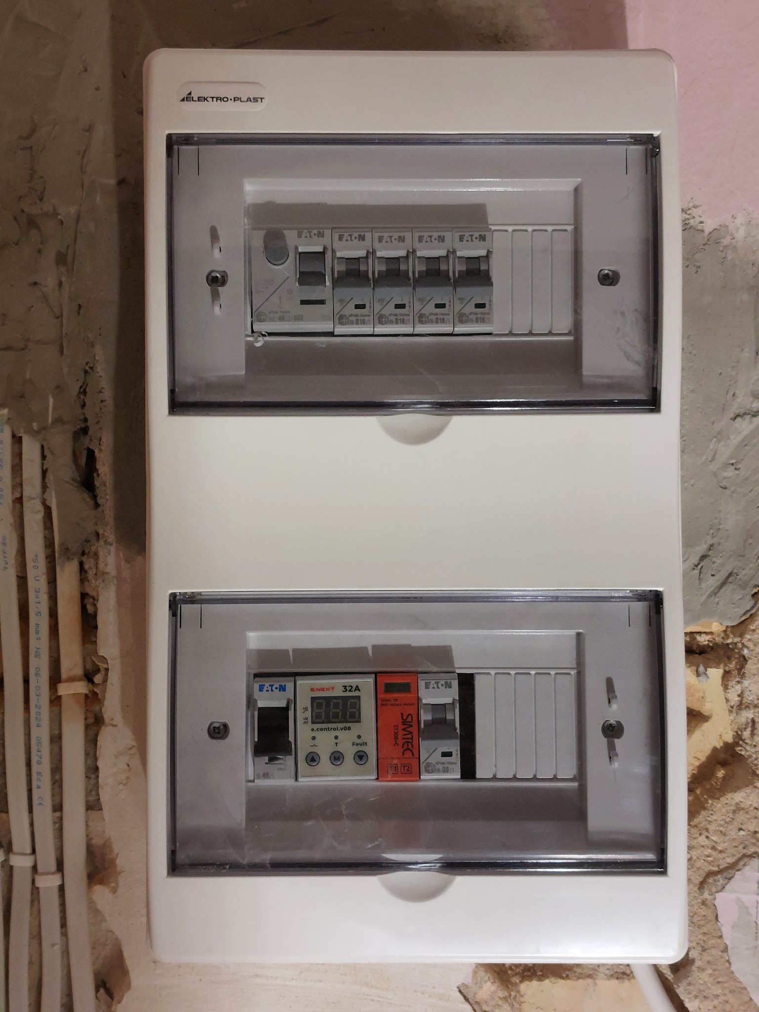 Rozdzielnica elektryczna firmy Elektro-Plast z zainstalowanymi bezpiecznikami Eaton i modułem sterującym ENEXT 32A, zamontowana na surowej ścianie.