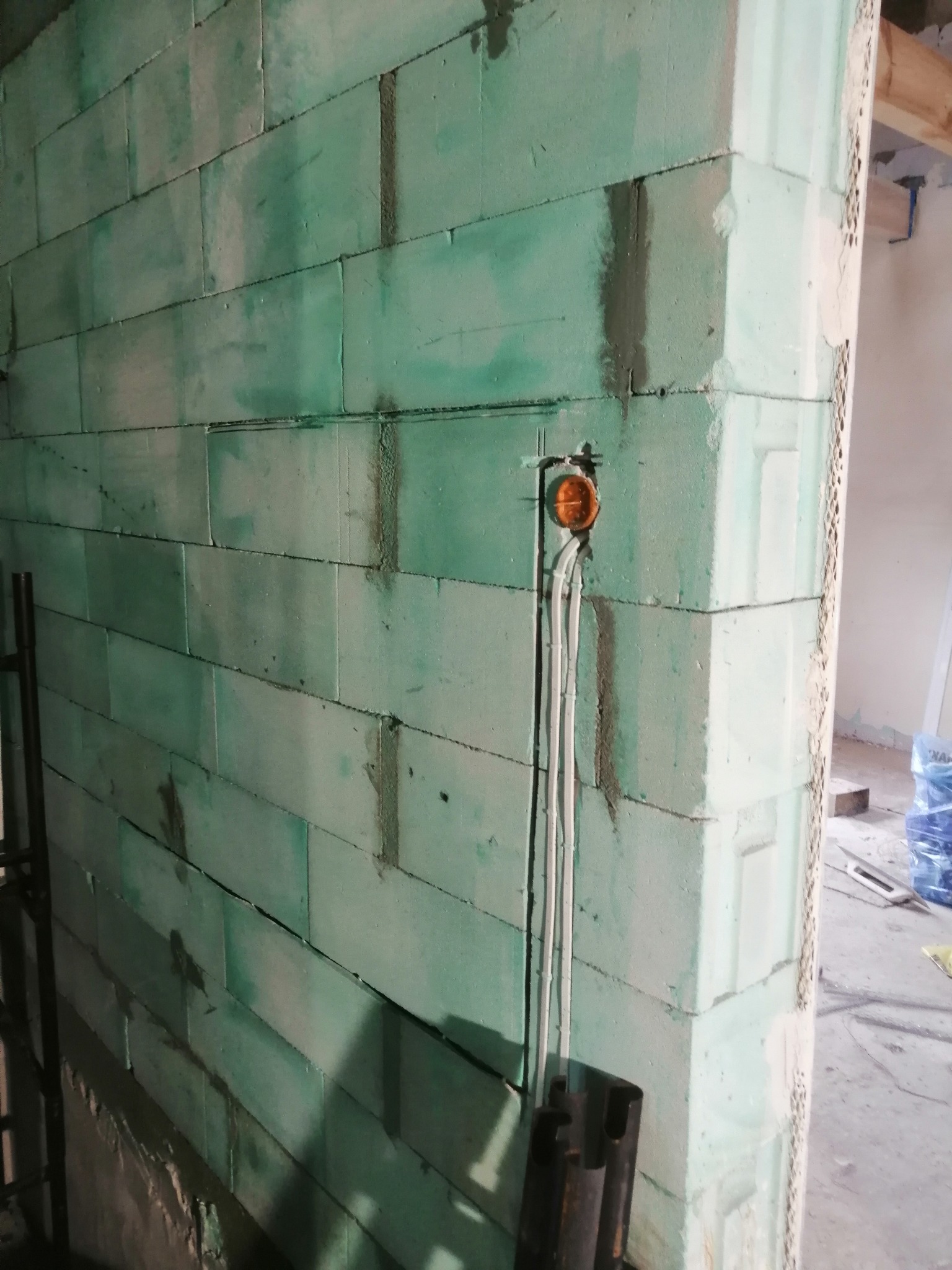 Ściana z betonu komórkowego w trakcie budowy z widoczną puszką instalacyjną i wystającymi przewodami elektrycznymi.