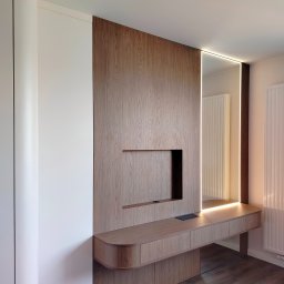 Nowoczesna zabudowa z drewna z podświetlanym lustrem i szafkami. Minimalistyczny design, ciepłe oświetlenie, drewniana podłoga. Detal wykończenia wnętrza.