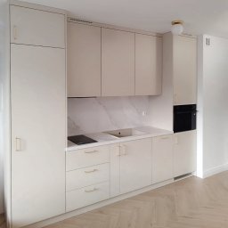 VS FURNITURE SPÓŁKA Z OGRANICZONĄ ODPOWIEDZIALNOŚCIĄ - Jasna zabudowa kuchenna z beżowymi frontami i złotymi uchwytami, marmurowy backsplash, płyta indukcyjna i piekarnik w wysokiej zabudowie. Parkiet w jodełkę na podłodze.