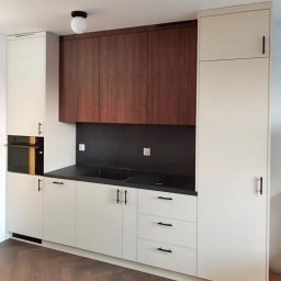 VS FURNITURE SPÓŁKA Z OGRANICZONĄ ODPOWIEDZIALNOŚCIĄ - Nowoczesna kuchnia z białymi szafkami i drewnianymi górnymi szafkami. Czarny blat i backsplash. Parkiet w jodełkę na podłodze. Minimalistyczny design.