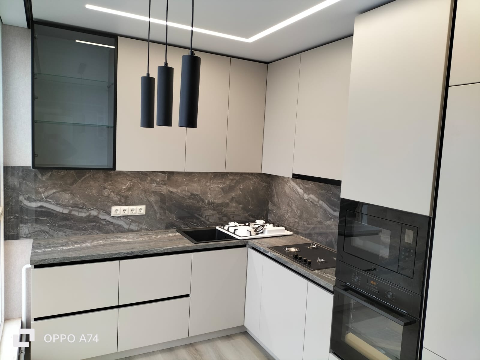 Nowoczesna kuchnia w odcieniach szarości i bieli z marmurowym blatem, oświetleniem LED i czarnymi wiszącymi lampami cylindrycznymi.