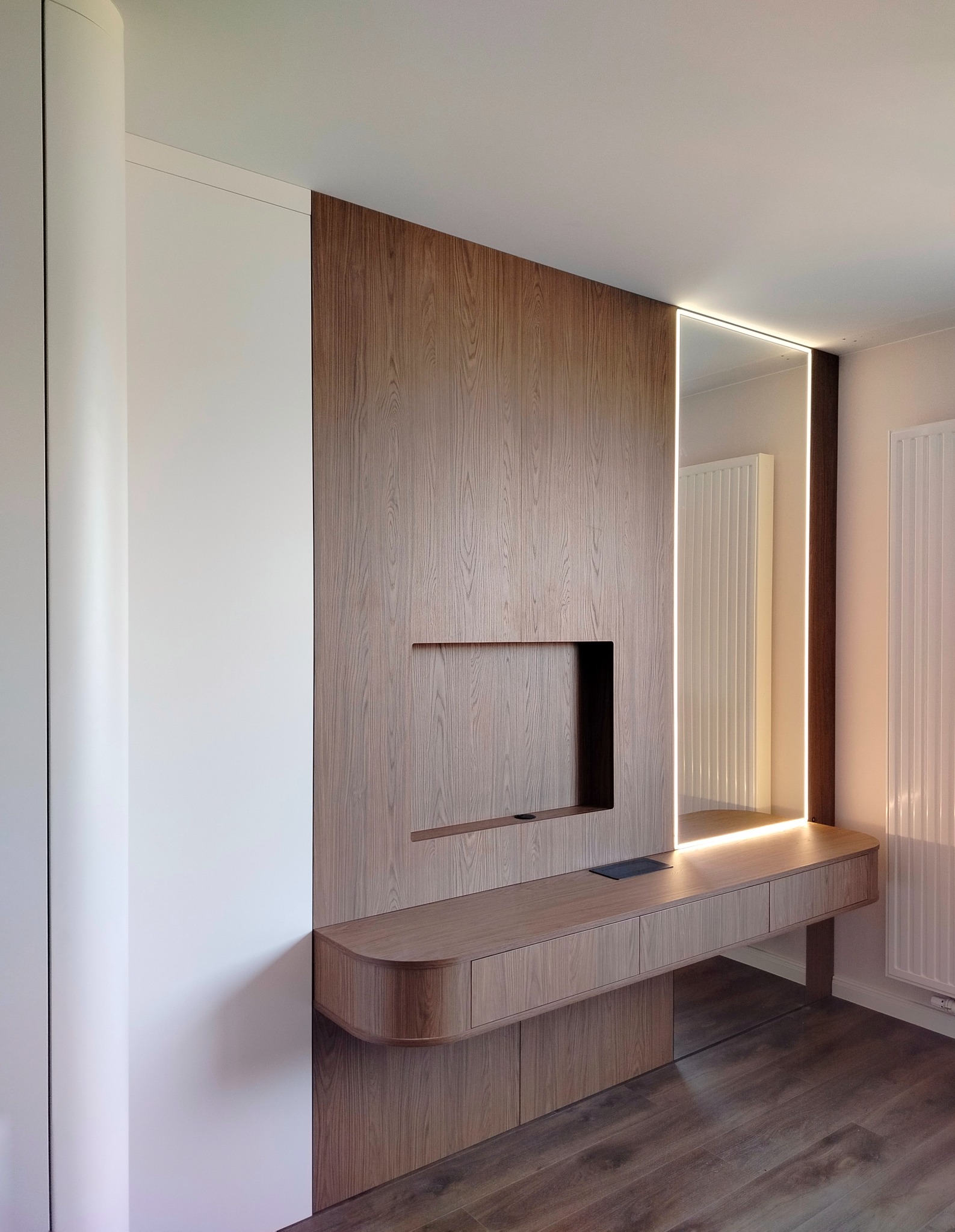 Nowoczesna zabudowa z drewna z podświetlanym lustrem i szafkami. Minimalistyczny design, ciepłe oświetlenie, drewniana podłoga. Detal wykończenia wnętrza.