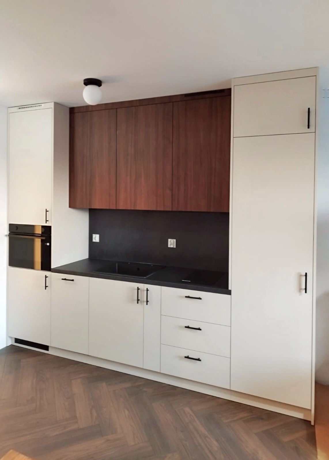 Nowoczesna kuchnia z białymi szafkami i drewnianymi górnymi szafkami. Czarny blat i backsplash. Parkiet w jodełkę na podłodze. Minimalistyczny design.