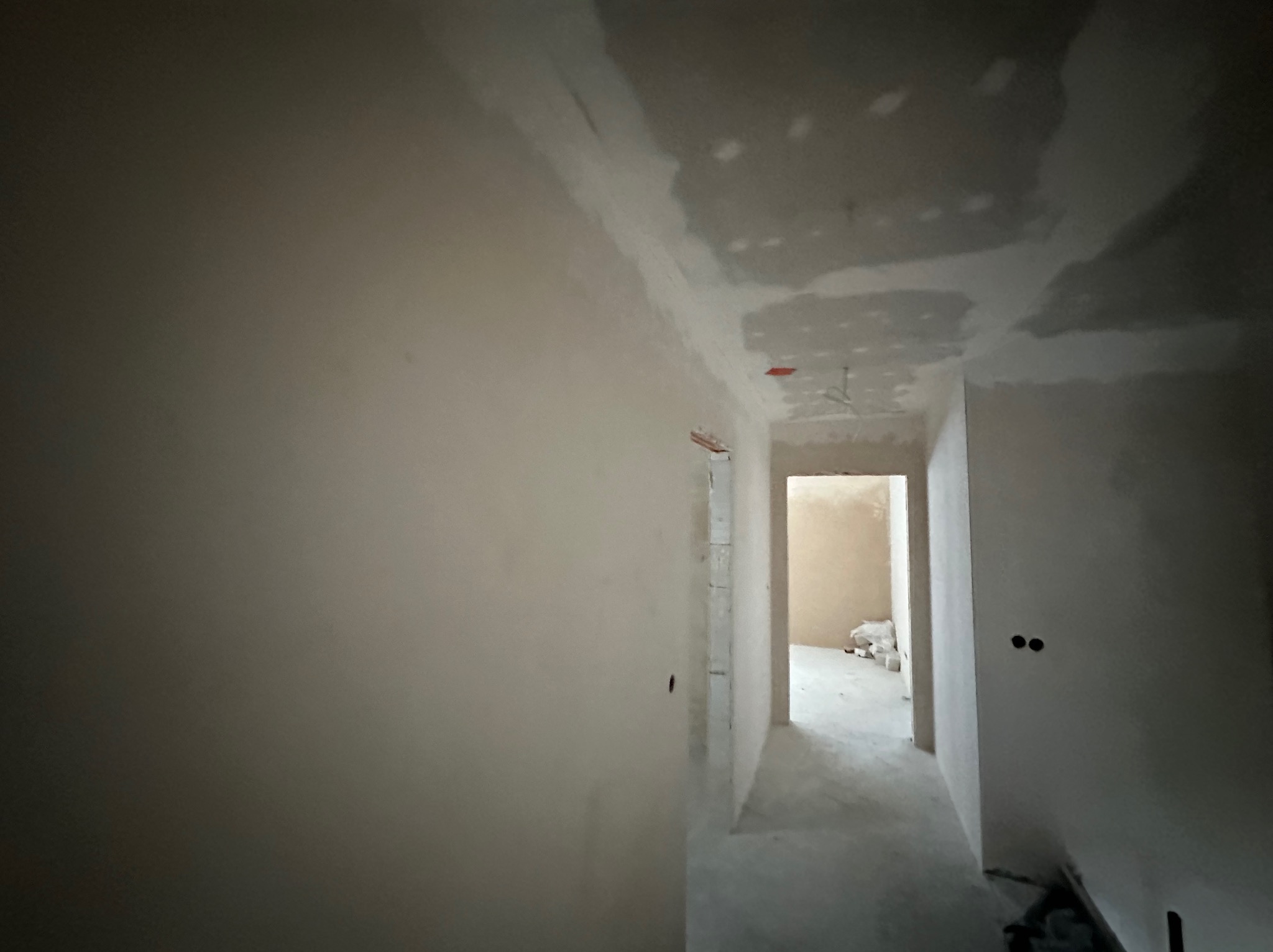 Wnętrze w trakcie prac wykończeniowych: ściany po szpachlowaniu, widoczne nierówności i przygotowanie do dalszych etapów. Otwór drzwiowy w perspektywie.