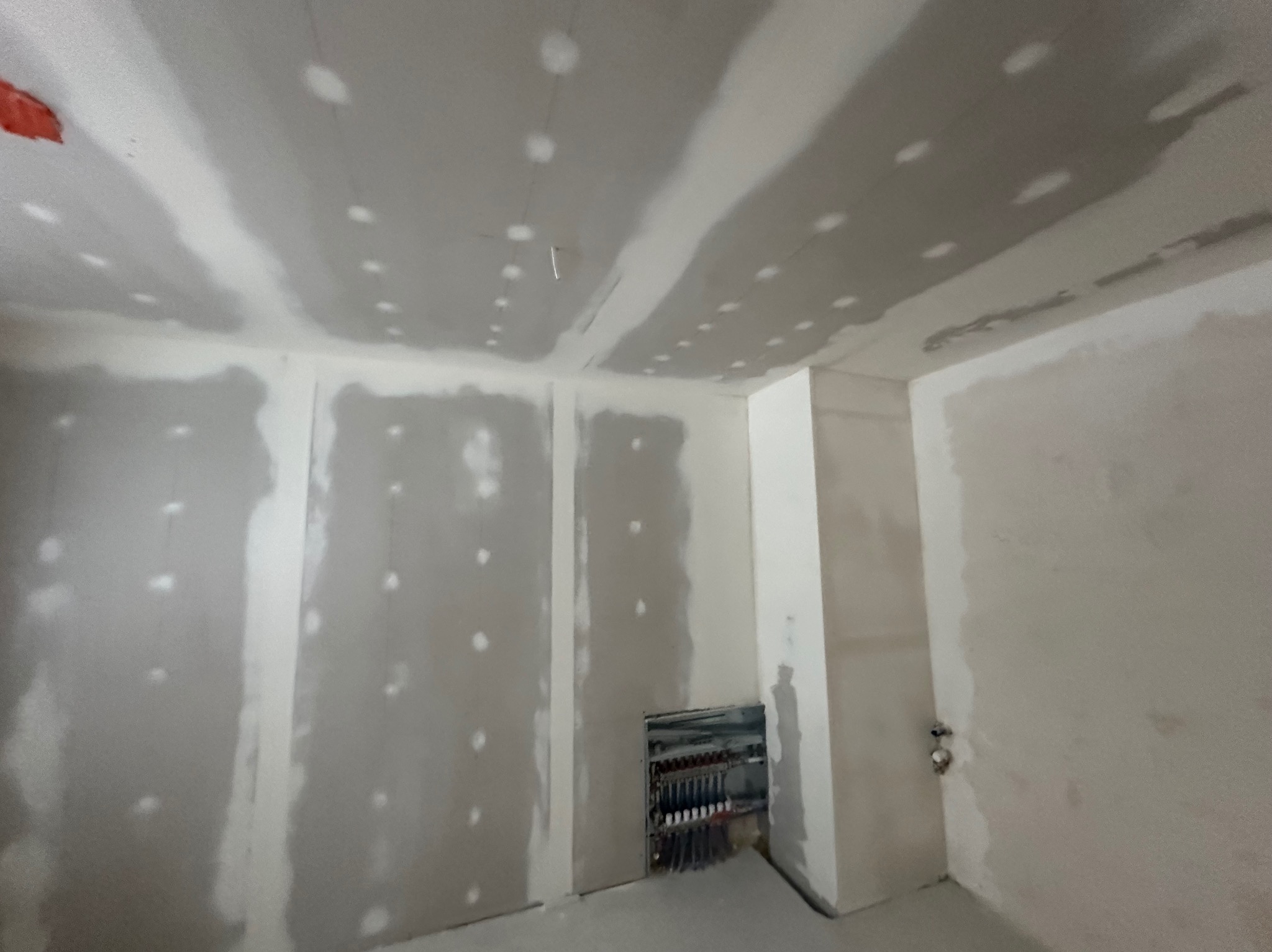 Wnętrze w trakcie prac wykończeniowych: ściany i sufit pokryte szpachlą, widoczne punkty mocowań, instalacja elektryczna w ścianie. Surowy stan przed malowaniem.