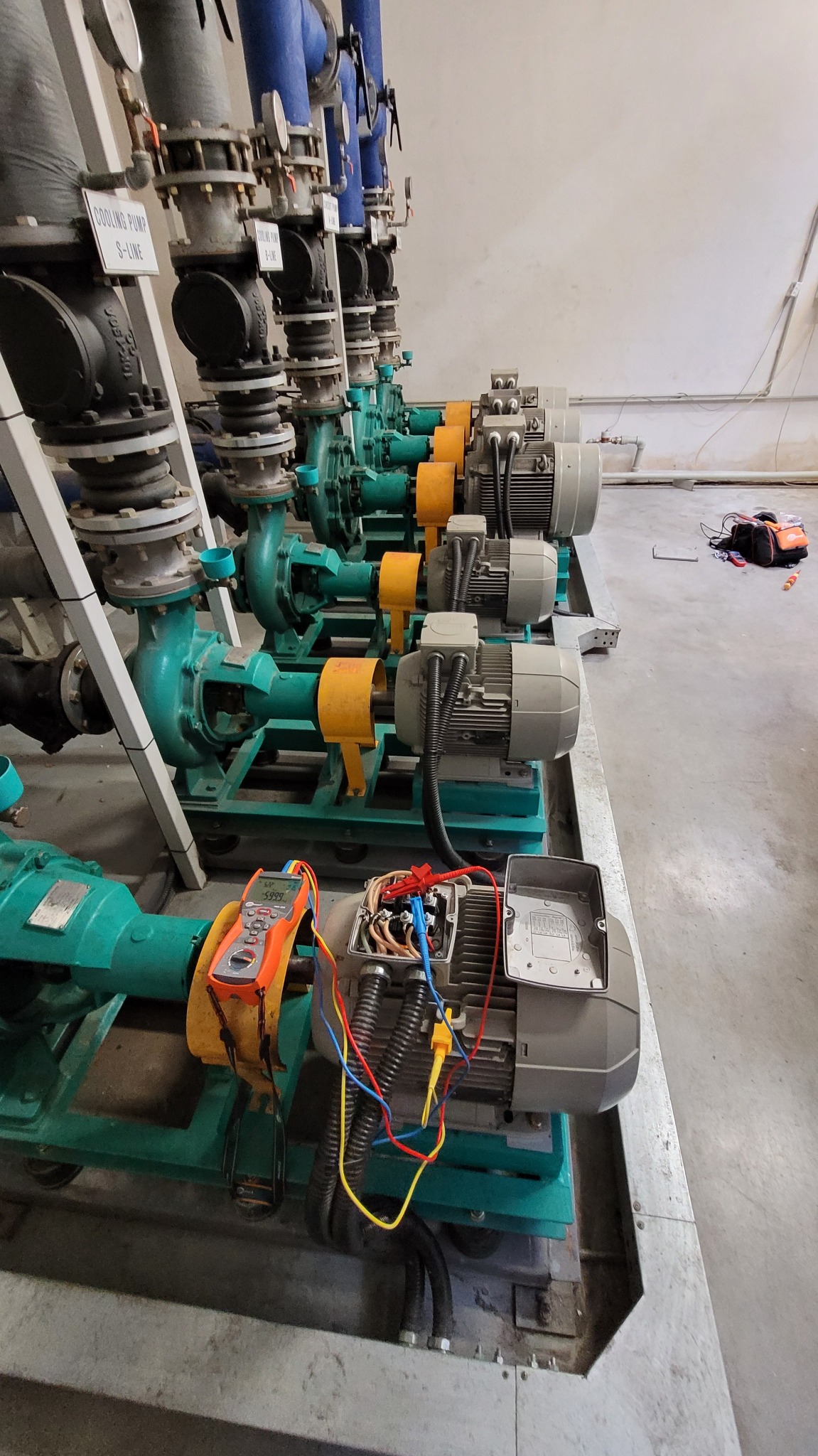 Pomiary rezystancji uzwojeń silnika pompy chłodzenia, multimetr cyfrowy z przewodami pomiarowymi, otwarty panel elektryczny silnika z widocznymi kablami.