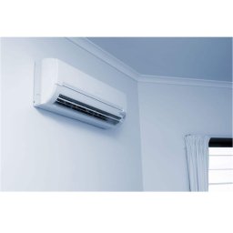 MULTIMAKE SPÓŁKA Z OGRANICZONĄ ODPOWIEDZIALNOŚCIĄ - Biały klimatyzator ścienny zamontowany w rogu pokoju, widoczne białe ściany, sufit z listwami oraz okno z zasłoną.