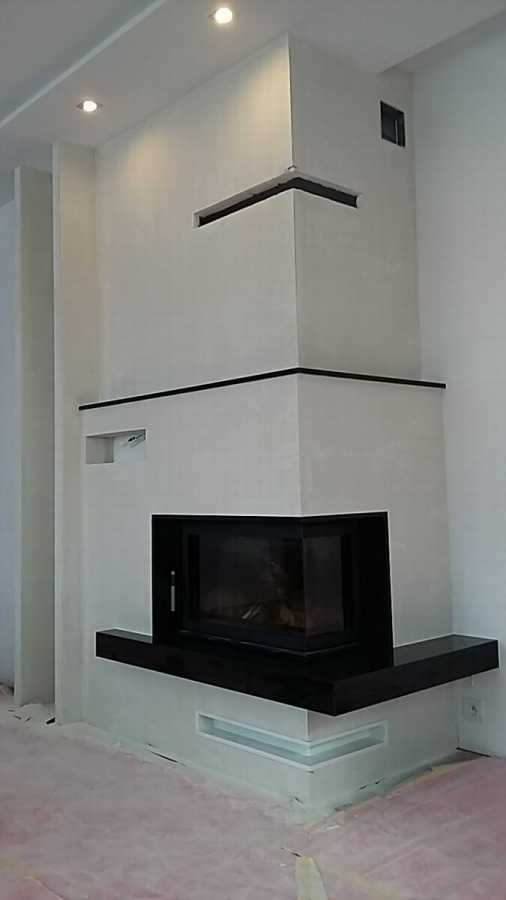 Nowoczesny narożny kominek z czarnymi akcentami, w trakcie wykończenia, z widocznym zabezpieczeniem podłogi folią.