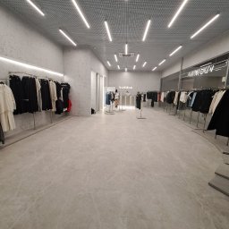 Kapitoshka - Wnętrze jasnego sklepu odzieżowego z ubraniami na wieszakach, gładka podłoga z marmuru i oświetlenie sufitowe