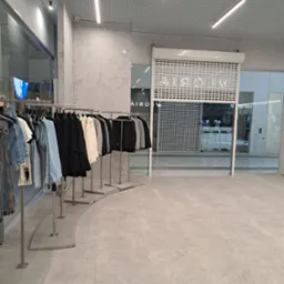 Jasne, minimalistyczne wnętrze sklepu odzieżowego z ubraniami na wieszakach i zamkniętą roletą antywłamaniową.