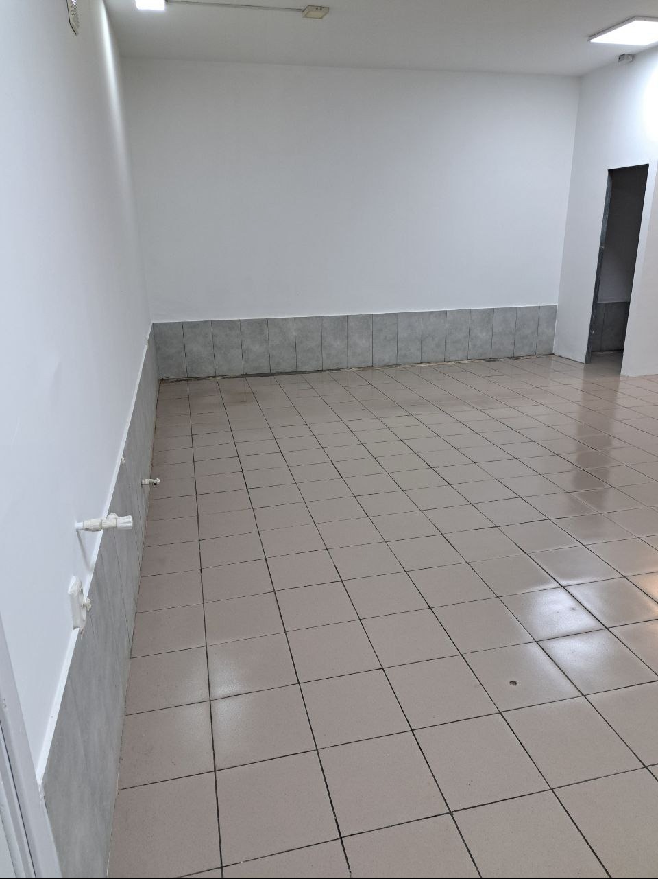 Puste pomieszczenie z beżowymi płytkami podłogowymi, szarą lamperią i białymi ścianami, przygotowane do użytku.