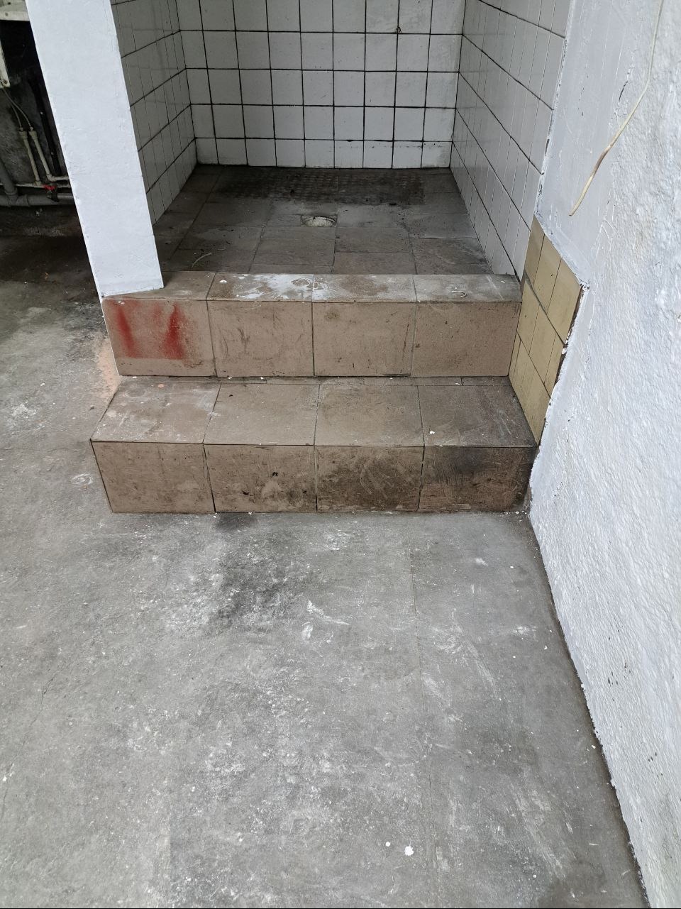 Brudny, kafelkowany brodzik z dwoma stopniami wejściowymi, ślady po remoncie.