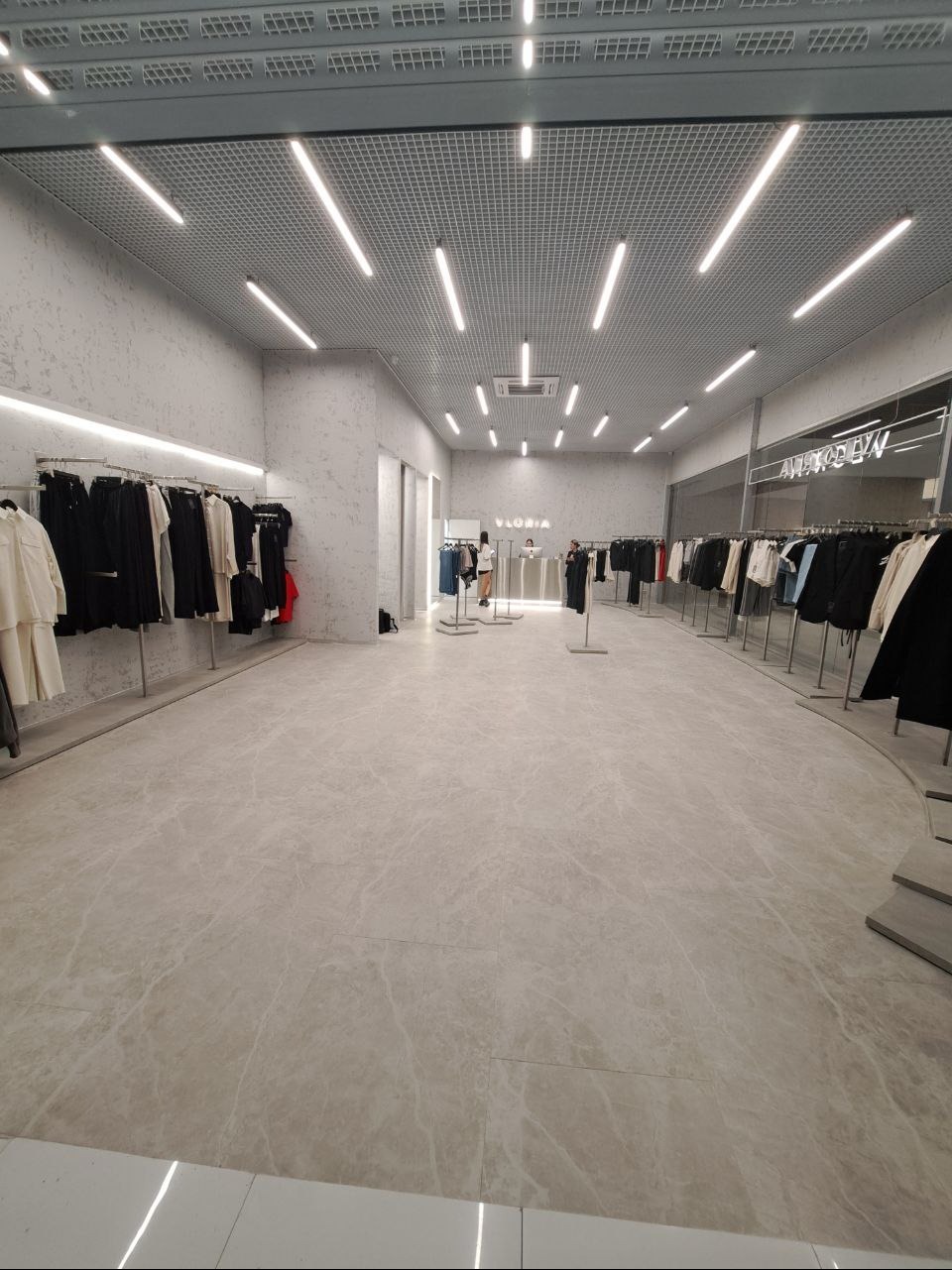 Wnętrze jasnego sklepu odzieżowego z ubraniami na wieszakach, gładka podłoga z marmuru i oświetlenie sufitowe