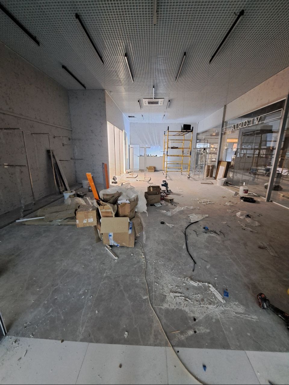 Wnętrze lokalu w trakcie wykańczania: kartony, gruz na podłodze, drabina rusztowaniowa w tle, surowy beton na ścianach.