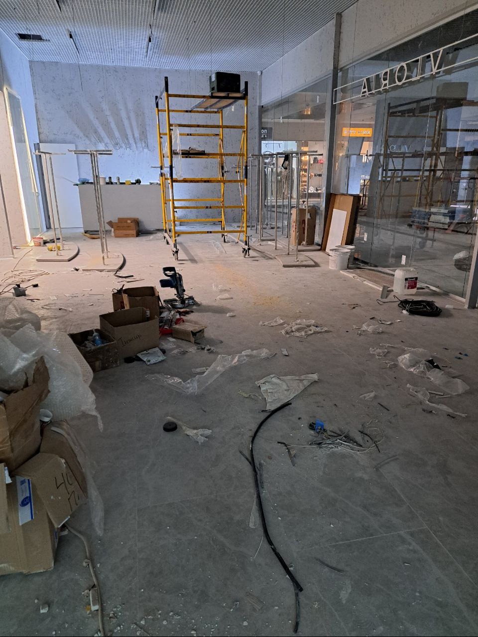Wnętrze sklepu w trakcie remontu: rozstawione rusztowanie, narzędzia, kartony i resztki materiałów budowlanych na podłodze.