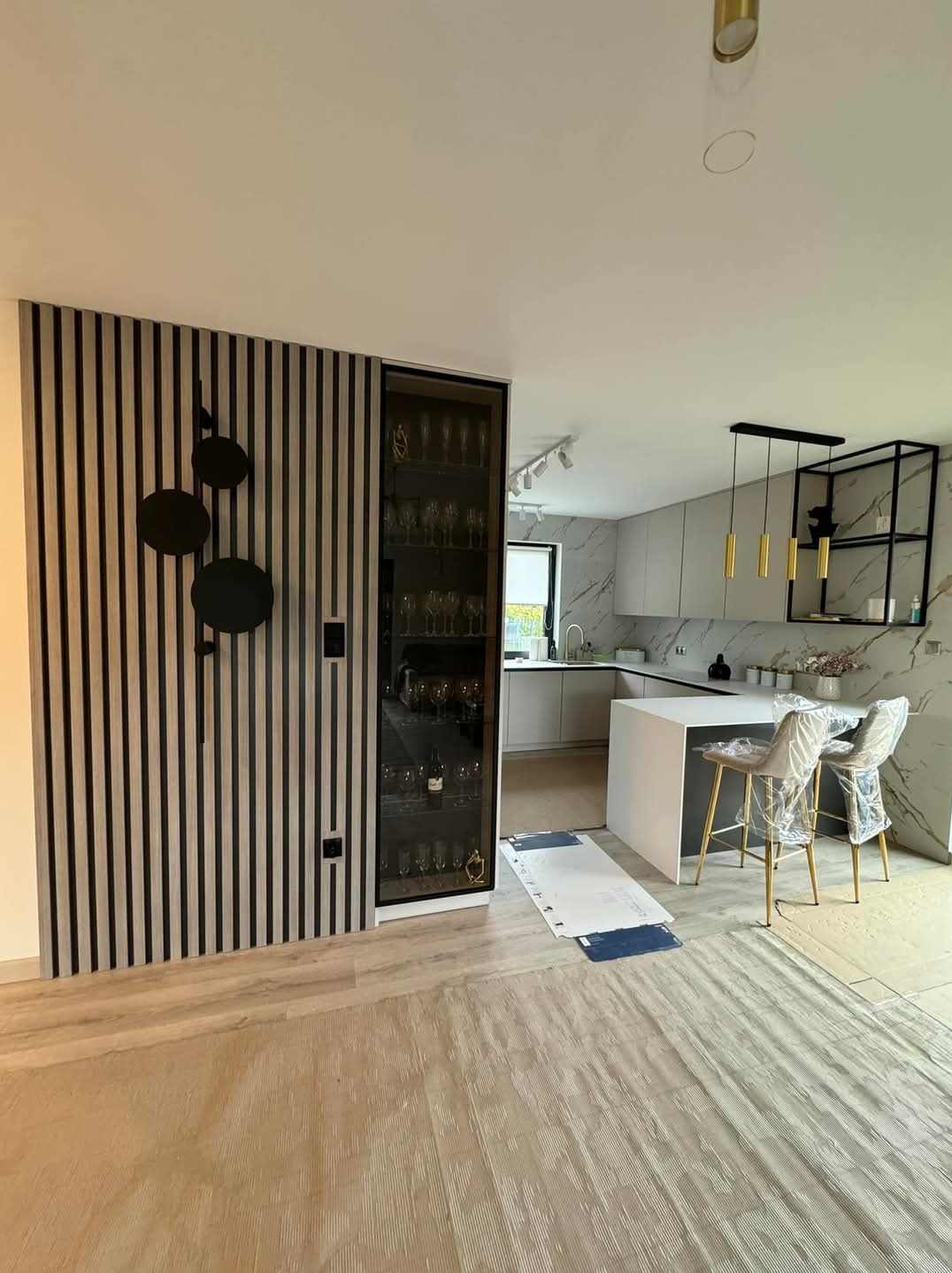 Nowoczesna kuchnia z zabudowaną szafą na alkohole, wykończona pionowymi panelami ściennymi z dekoracją w kształcie nut, krzesła barowe jeszcze w folii ochronnej.