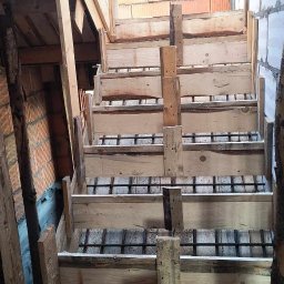 Nikolas słomski - Formowanie drewniane pod schody betonowe, widoczne zbrojenie stalowe, w tle ściana z czerwonej cegły dziurawki i ściana z białych bloczków gazobetonowych.