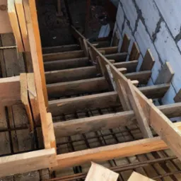 Szalunek schod&oacute;w w trakcie budowy, widoczne zbrojenie i fragment murowanej ściany z bloczk&oacute;w. Drewniane elementy konstrukcji tymczasowej.