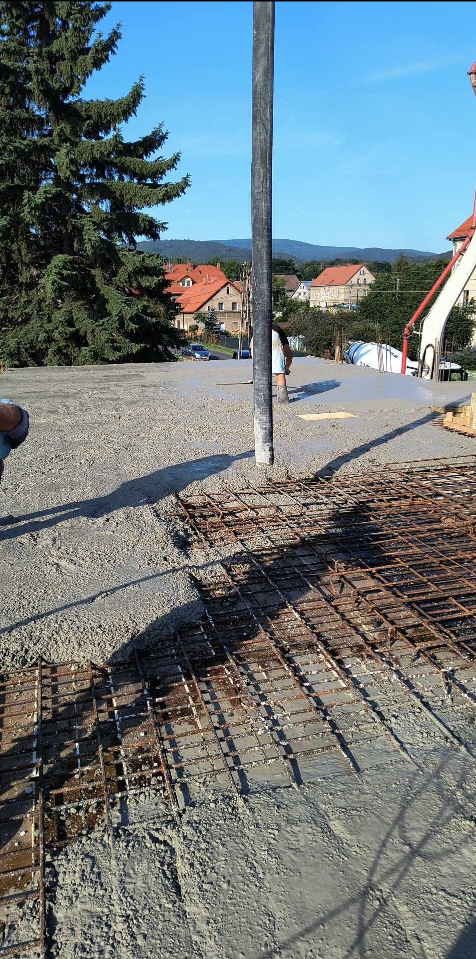 Wylewanie betonu na zbrojenie fundamentu domu jednorodzinnego, widoczna pompa do betonu, domy w tle.