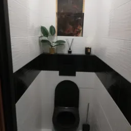 Nowoczesna toaleta z białymi, falistymi płytkami ściennymi, czarnym pasem dekoracyjnym, czarną armaturą i marmurową podłogą, uzupełniona o roślinę doniczkową i akcesoria zapachowe na półce.