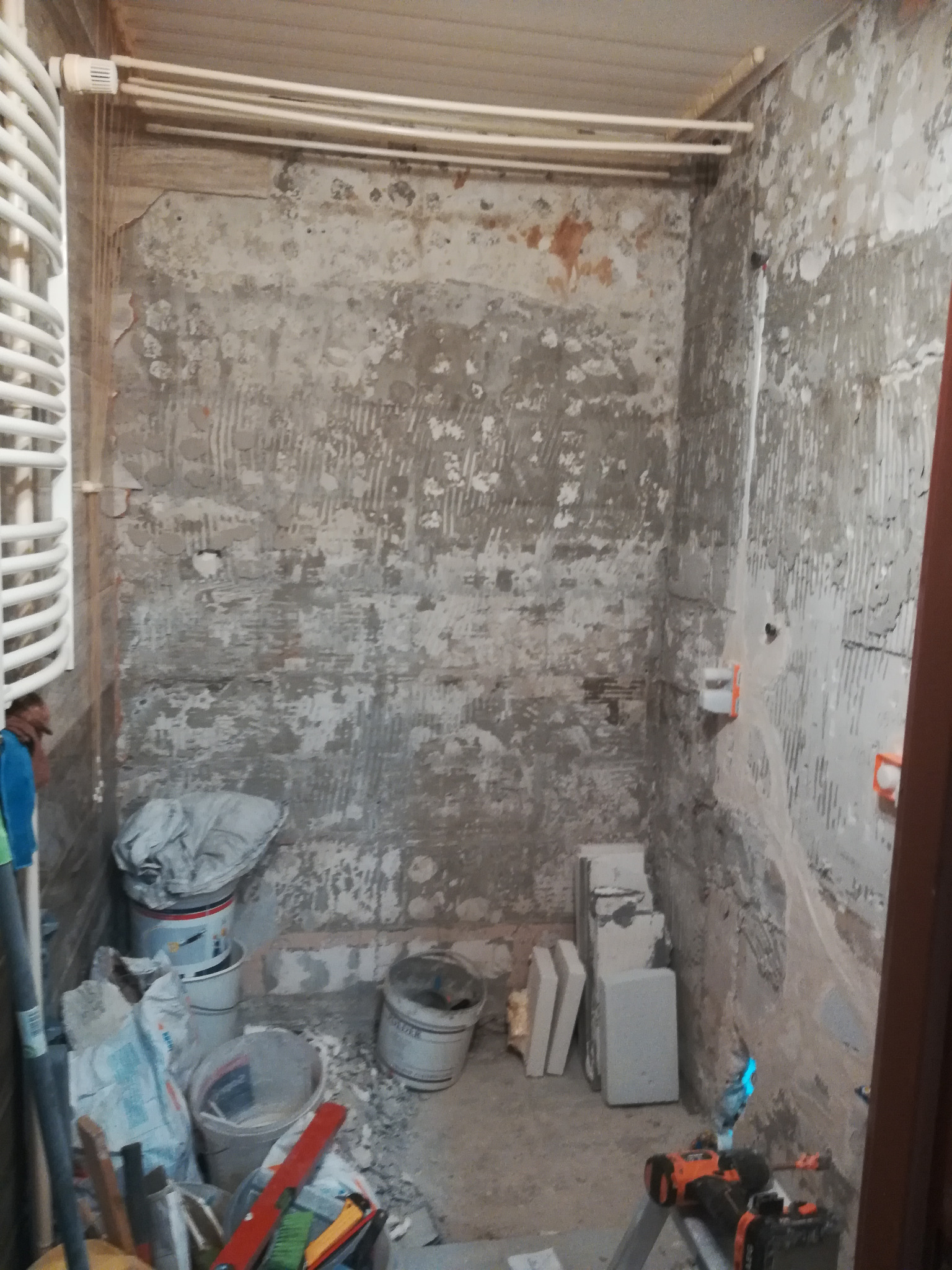 Łazienka w trakcie przygotowania do remontu: ściany bez płytek, widoczne warstwy podłoża, narzędzia i materiały budowlane w pomieszczeniu.