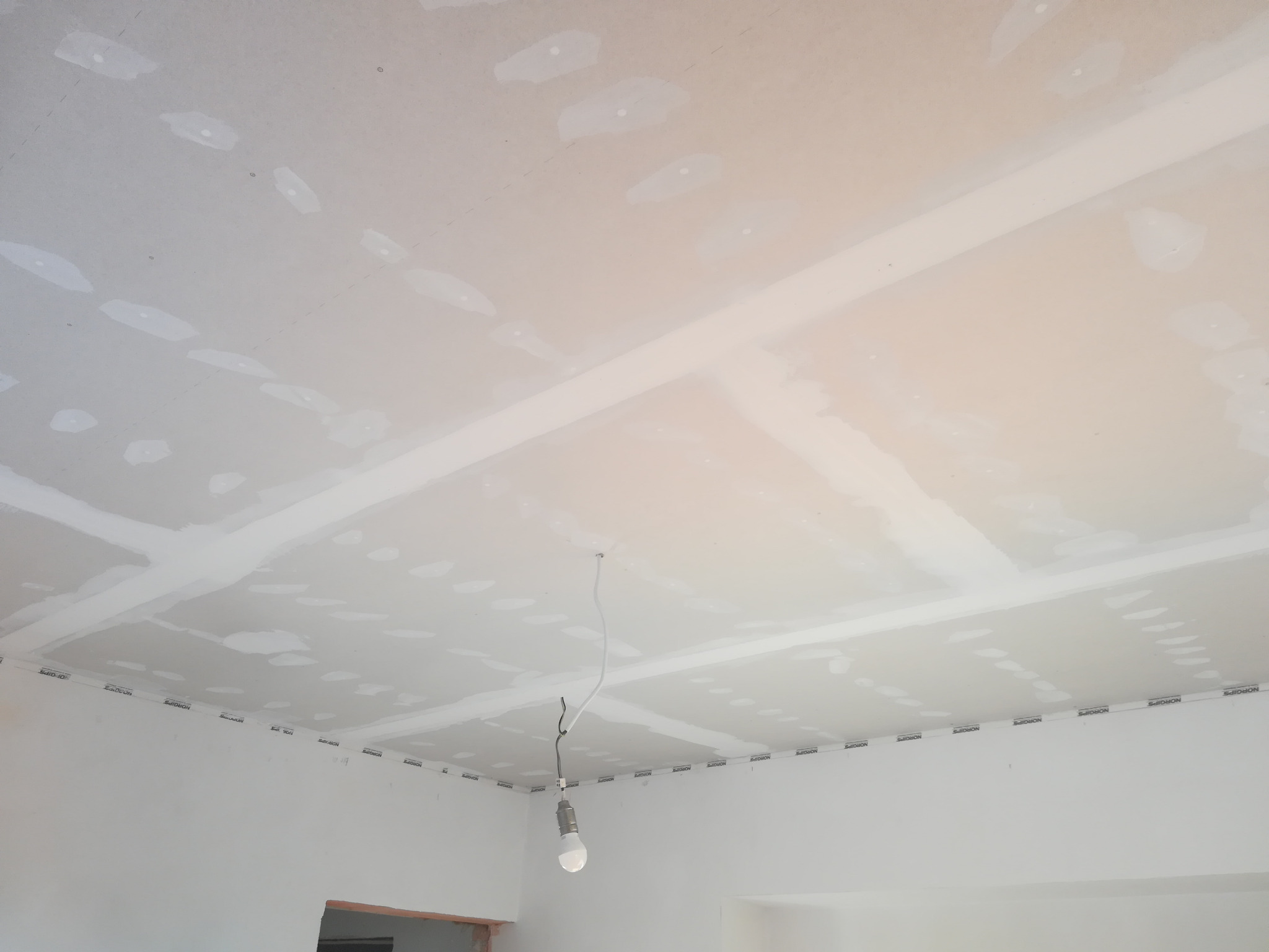 Sufit podwieszany z płyt gipsowo-kartonowych w trakcie prac wykończeniowych w Białymstoku, widoczne łączenia płyt wymagające szpachlowania, wisząca żarówka tymczasowa.