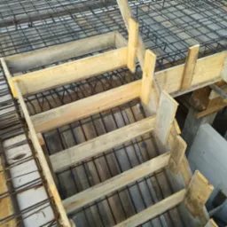 Zbrojenie stropu z drewnianym szalunkiem, widok z góry na konstrukcję w trakcie budowy z widocznymi elementami stalowymi i drewnianymi deskami.