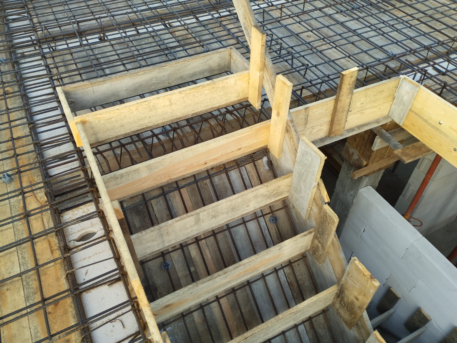 Zbrojenie stropu z drewnianym szalunkiem, widok z góry na konstrukcję w trakcie budowy z widocznymi elementami stalowymi i drewnianymi deskami.