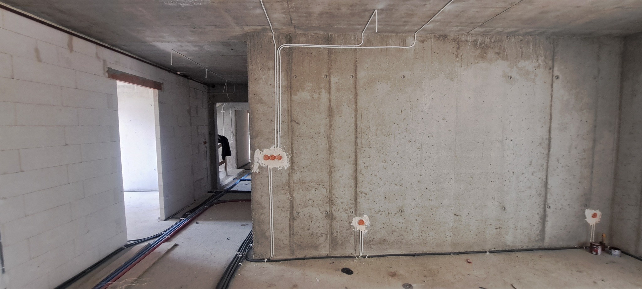 Surowy stan budynku w trakcie prac elektrycznych: widoczne kable prowadzone po ścianach i suficie, puszki elektryczne w ścianach, ściany z betonu i bloczków, podłoga w stanie surowym.
