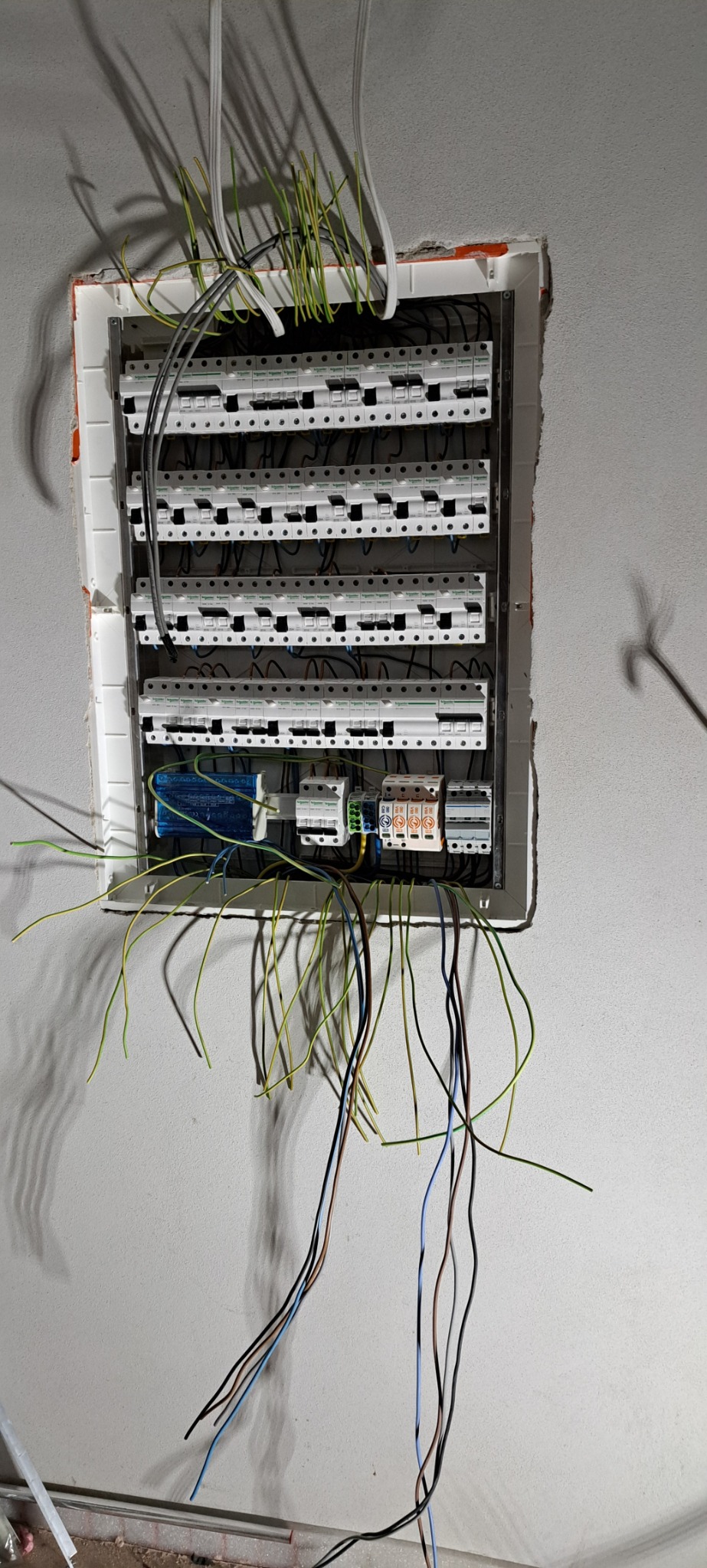 Rozdzielnia elektryczna w trakcie montażu, widoczne liczne bezpieczniki, kable w różnych kolorach oraz niedokończone wykończenie ściany wokół skrzynki.